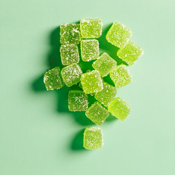 Green gummy candy cubes sprinkled with sugar on a pastel green background – vibrant, sweet, and chewy treat by Structure Formulations.