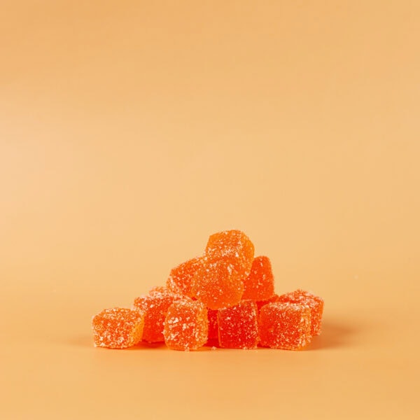 Vegan orange gummy candies with sugar coating on plain peach background.