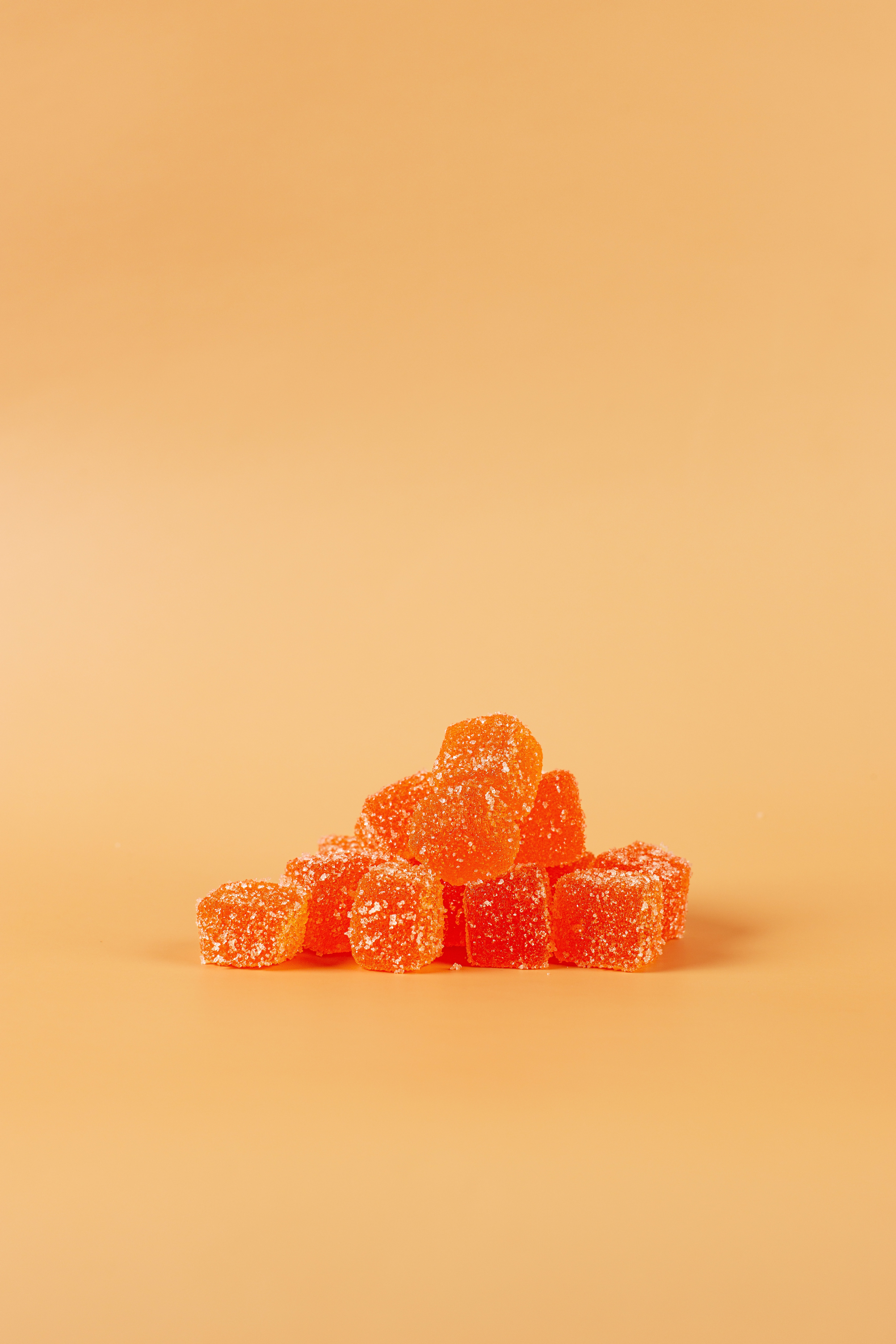 Vegan orange gummy candies with sugar coating on plain peach background.