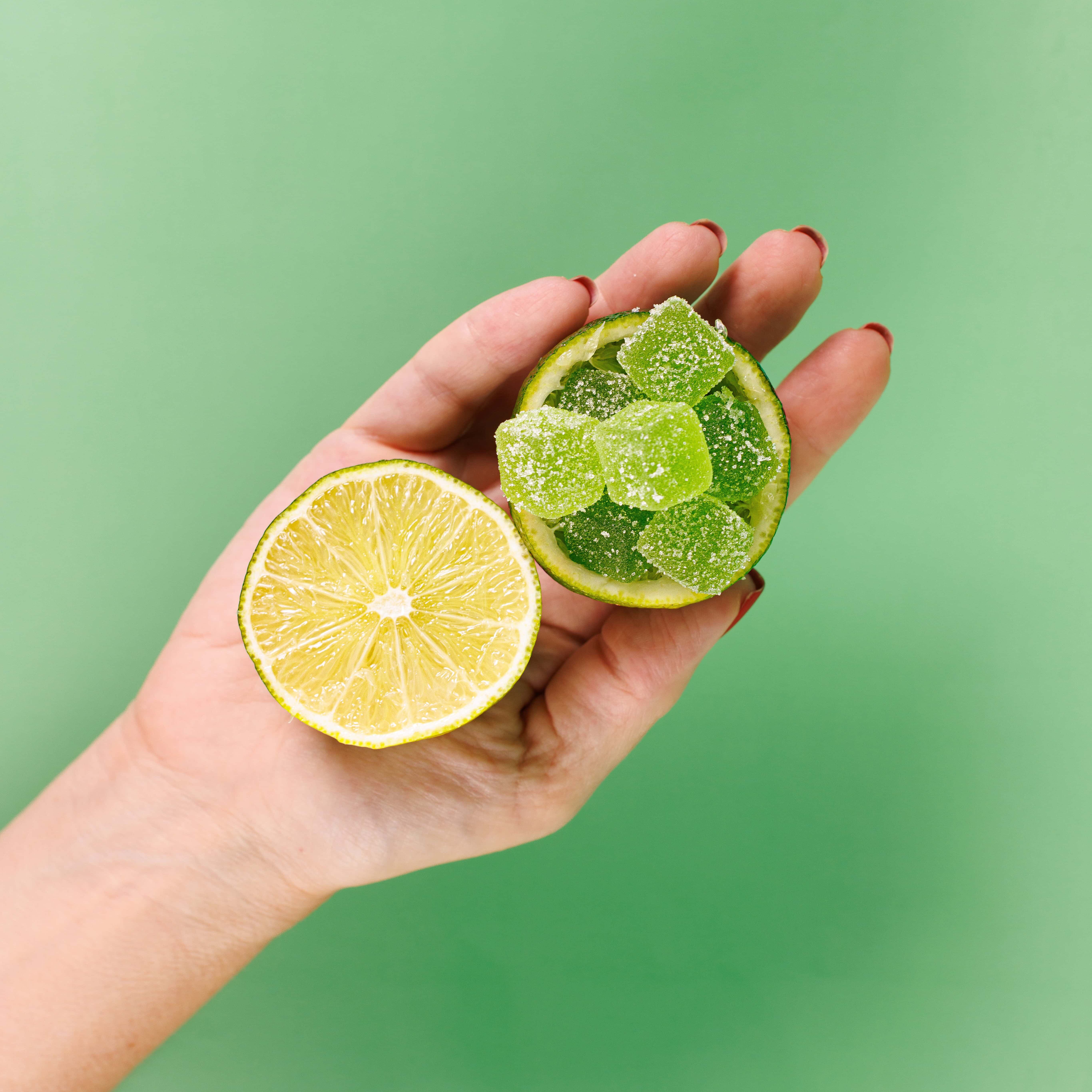 Fresh lemon and lime with green gummy candies in a halved lime on a green background.